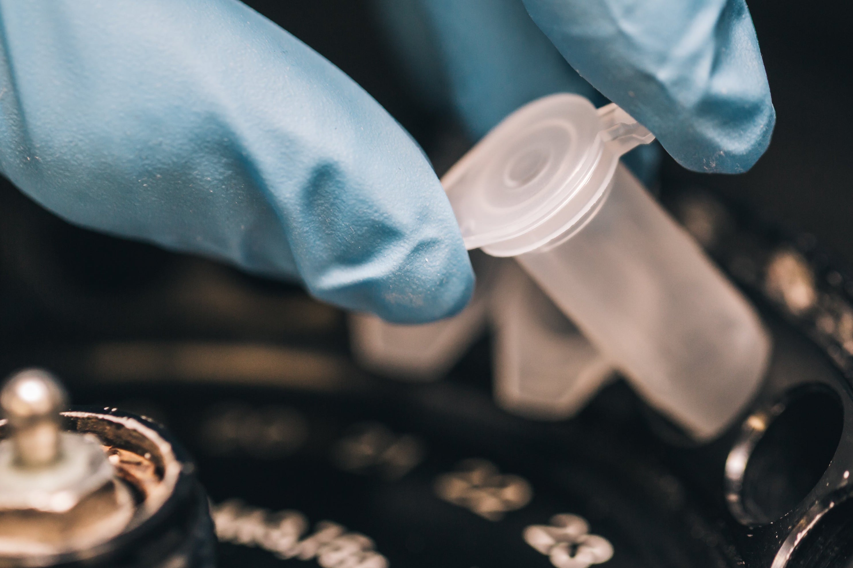 Person wearing blue gloves holding a small plastic component over a mechanical device.