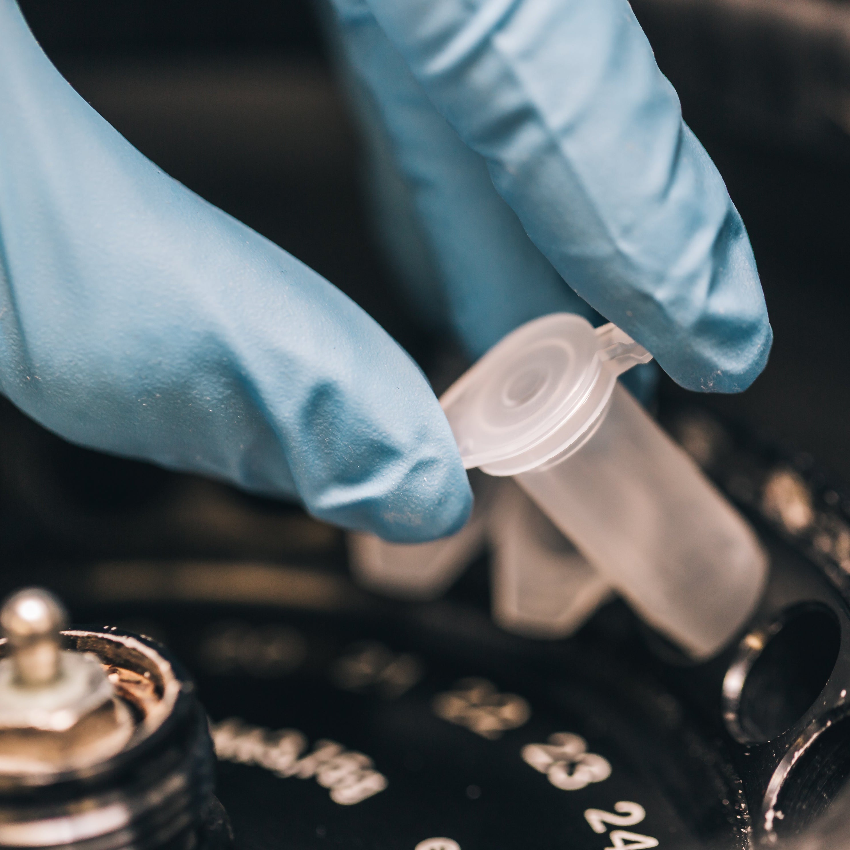 Person wearing blue gloves holding a small plastic component over a mechanical device.