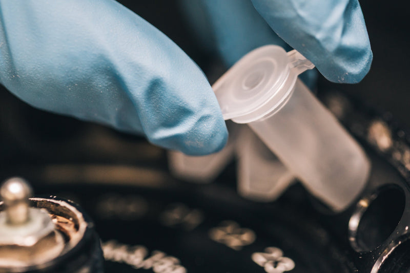Person wearing blue gloves holding a small plastic component over a mechanical device.
